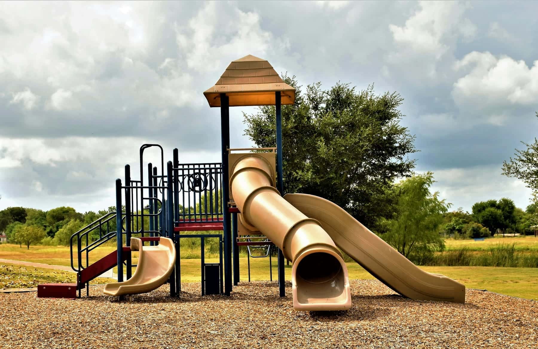 A play structure with a shingled roof and a long tube slide on an open field