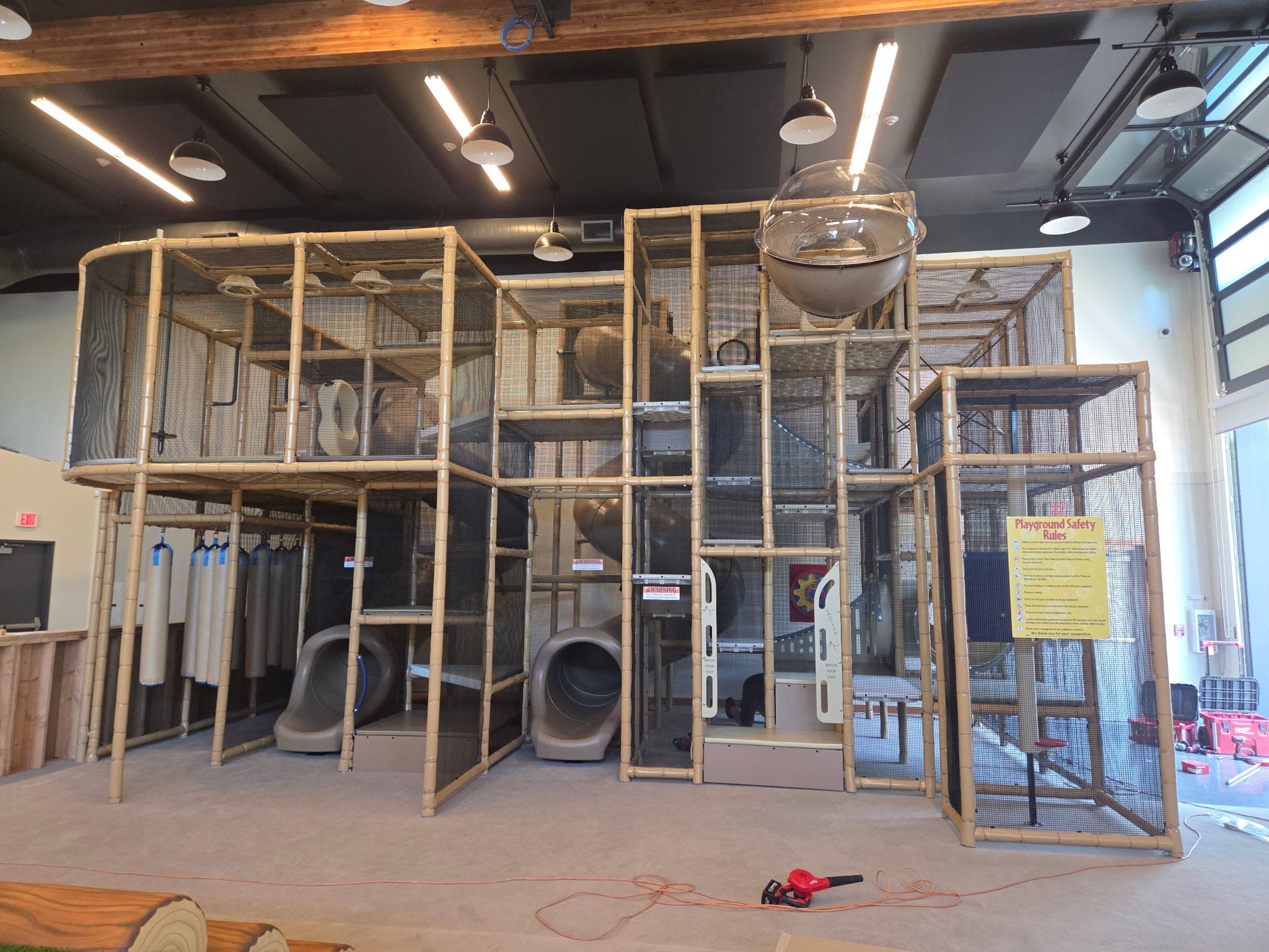 A new indoor playland we built: a two-level tan frame wrapped in netting, with tube slides, climbing tubes, and a clear bubble window on top